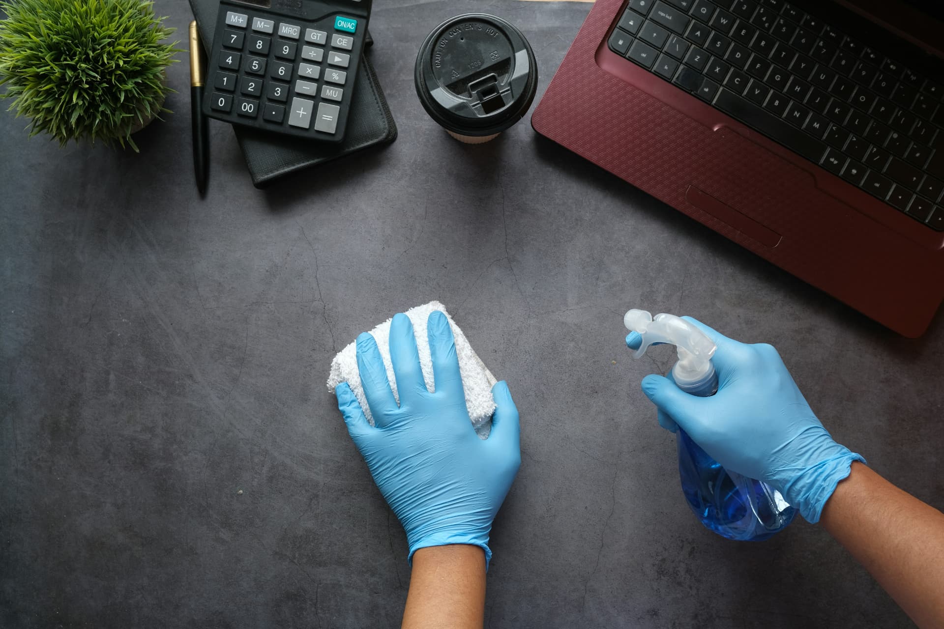 Gloved hands wiping down a dark office desk