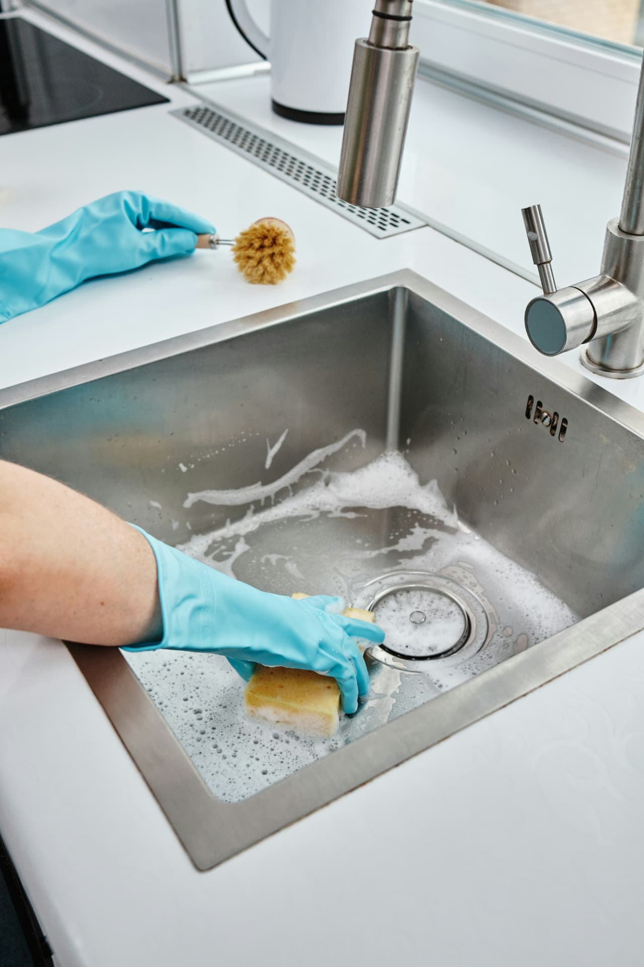 Cleaner washing a stainless steel sink with a sponge