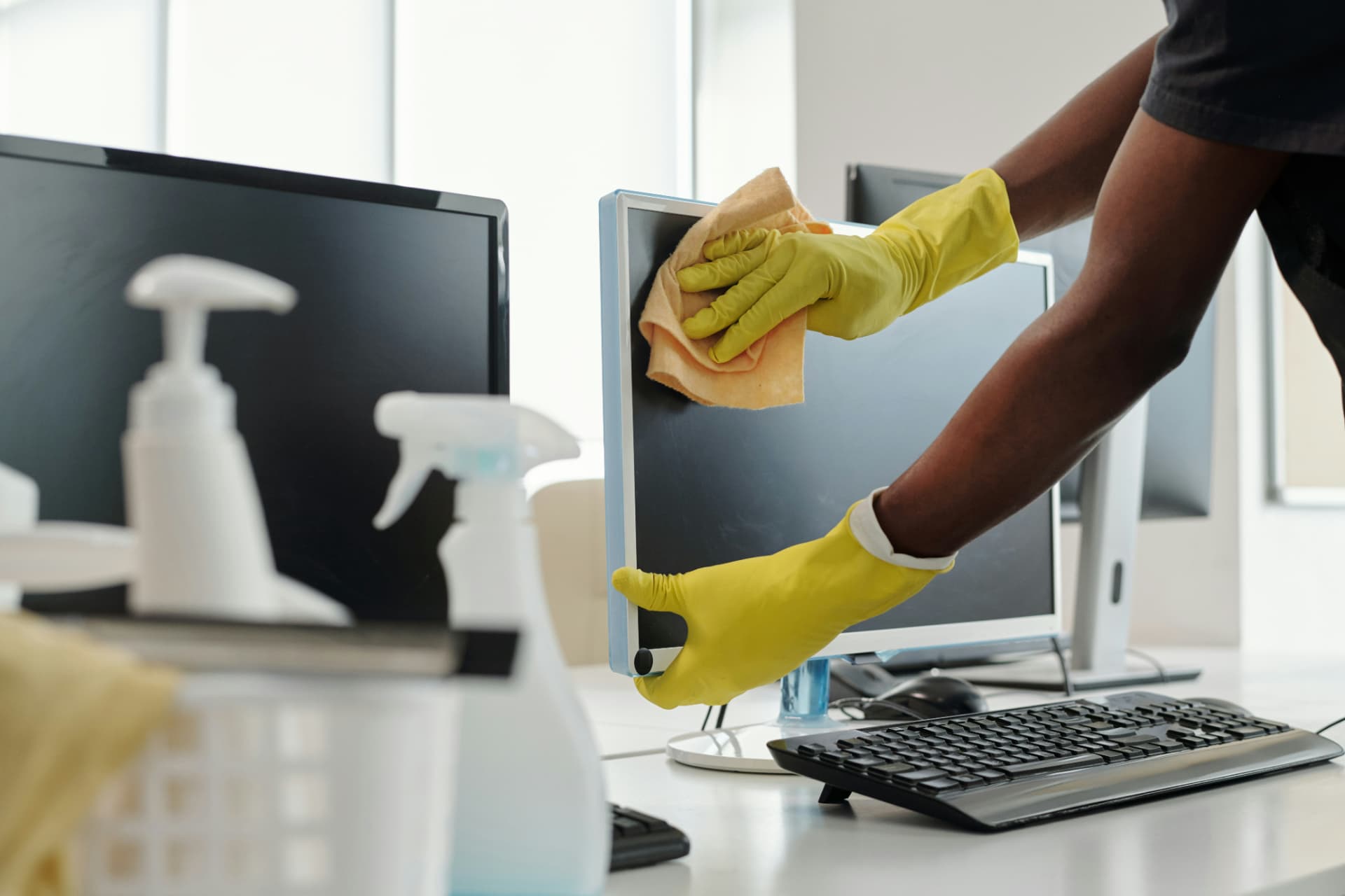 Cleaner wiping down a computer monitor in an office